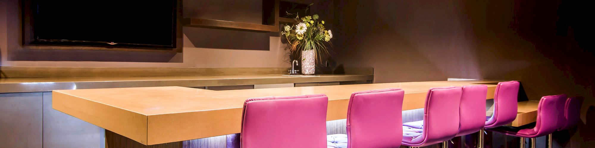 A modern bar area with purple barstools, wooden countertop, and a TV on the wall.