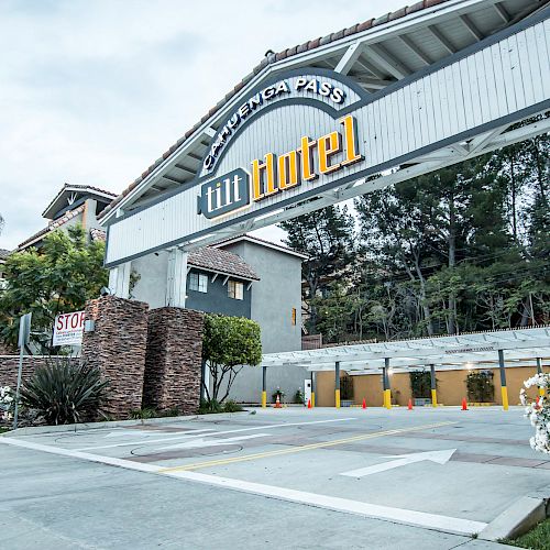 The image shows the entrance to the Tilt Hotel, featuring a modern design with stone pillars, greenery, and a visible 