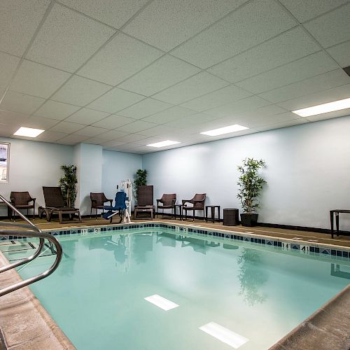 An indoor swimming pool surrounded by chairs and tables, plants against the walls, and a ceiling with fluorescent lights.