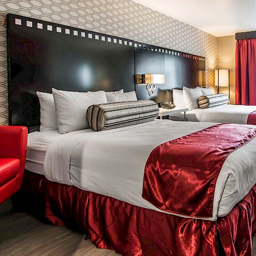 The image shows a hotel room with two double beds, red chairs, and modern decor featuring geometric patterns and red accents.