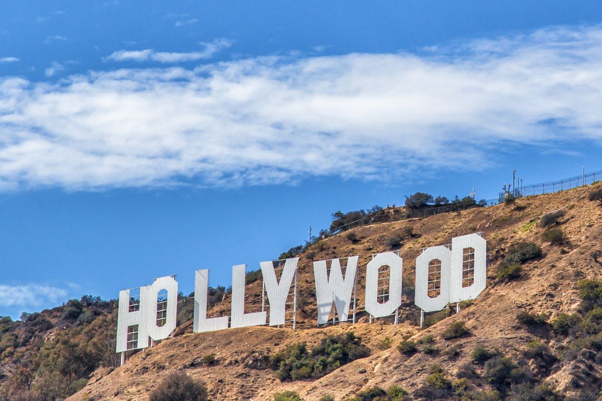 The image shows the iconic Hollywood sign situated on a hillside under a blue sky with some clouds.