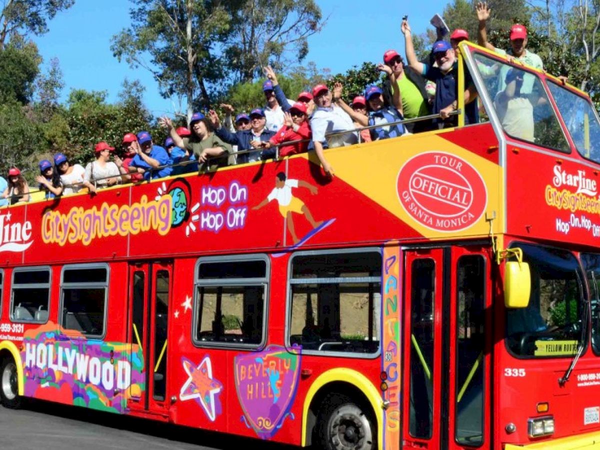 A red double-decker bus with an open top, labeled for city sightseeing, filled with people waving and taking photos.