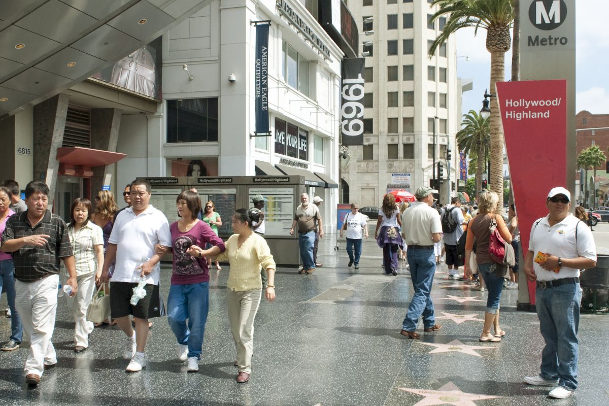 People walking on a sidewalk featuring stars along the Hollywood Walk of Fame, with shops and a Metro sign in the background.