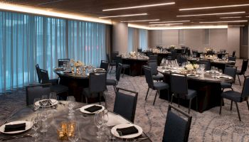 The image shows an elegantly set dining area with round tables adorned with glasses, plates, black napkins, and floral centerpieces.
