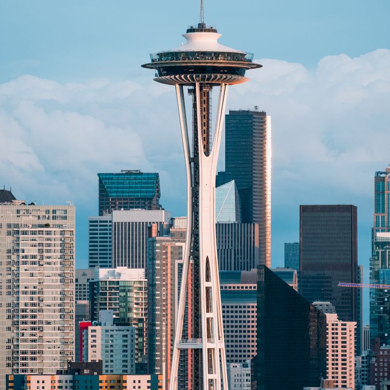The image shows a cityscape featuring the Space Needle with various high-rise buildings in the background against a partly cloudy sky.