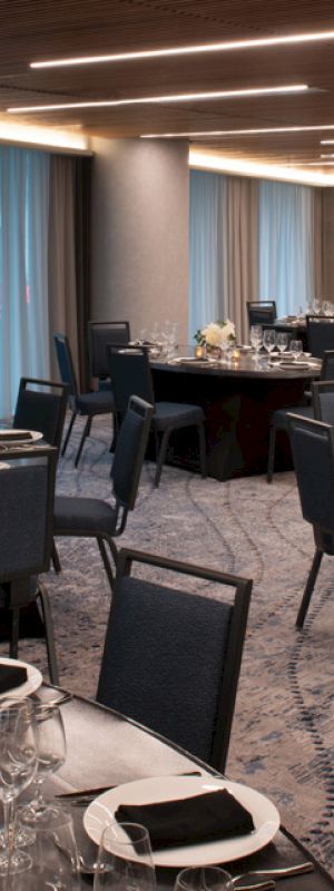 An elegantly set banquet hall with round tables and blue chairs, featuring floral centerpieces and napkin-folded table settings under soft ambient lighting.