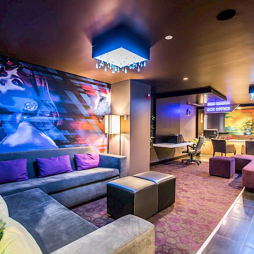 A modern, vibrant lounge with colorful artwork on the wall, plush seating, a reception area, and contemporary decor, including a chandelier.